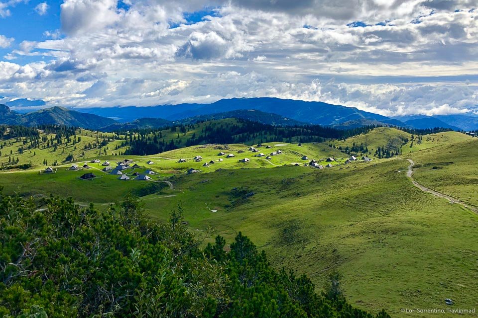 A view of a green hilly landscape with huts in the distance on Velika Planina in Slovenia