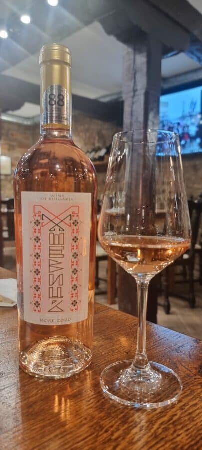 A bottle of pink wine next to a glass on a table in Veliko Tarnovo.