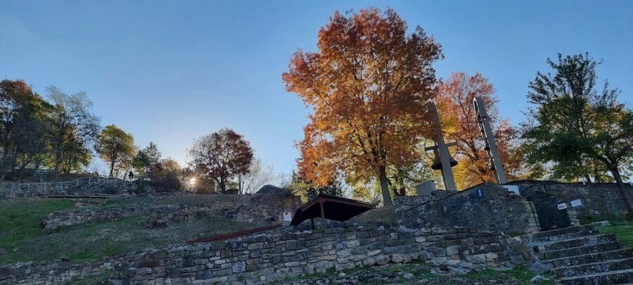 In the enchanting city of Veliko Tarnovo, the sun illuminates a majestic stone wall adorned with lush trees in the scenic background.